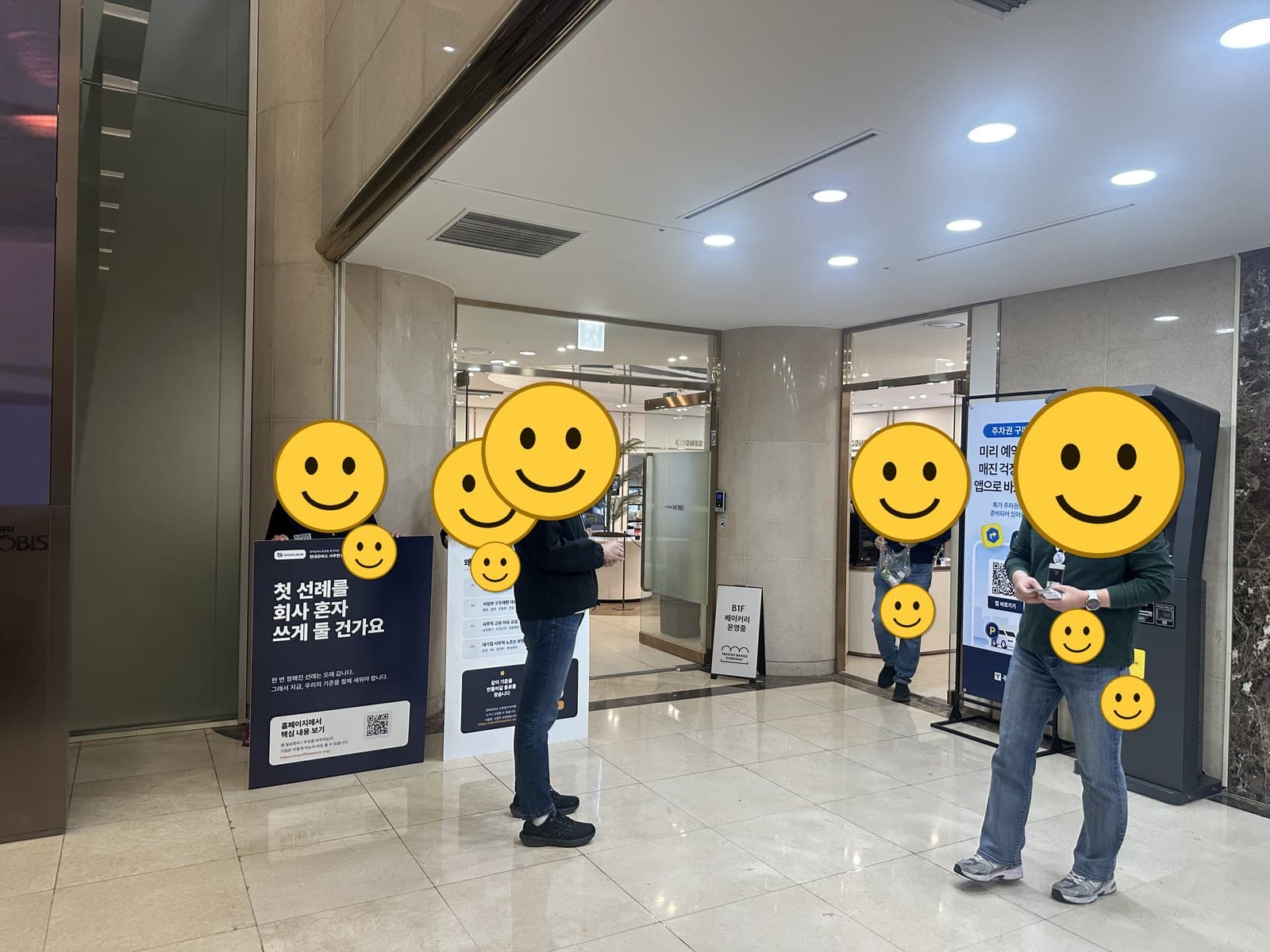 본사 로비 현장 홍보 — 조합원 얼굴과 사원증은 스마일 이모지로 가림 처리