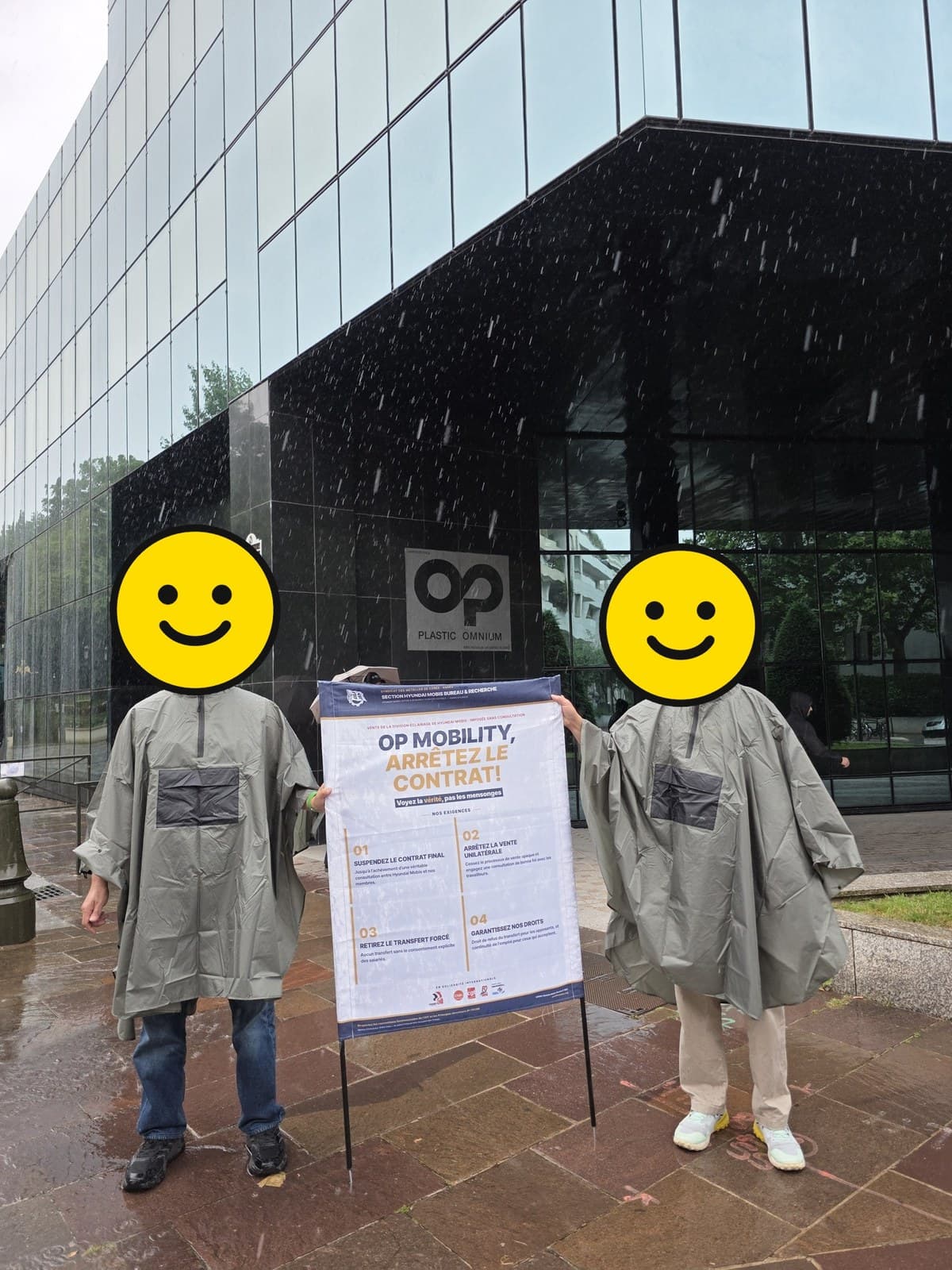 비 오는 날 우비를 입고 OP모빌리티 본사 앞에서 현수막을 든 두 조합원