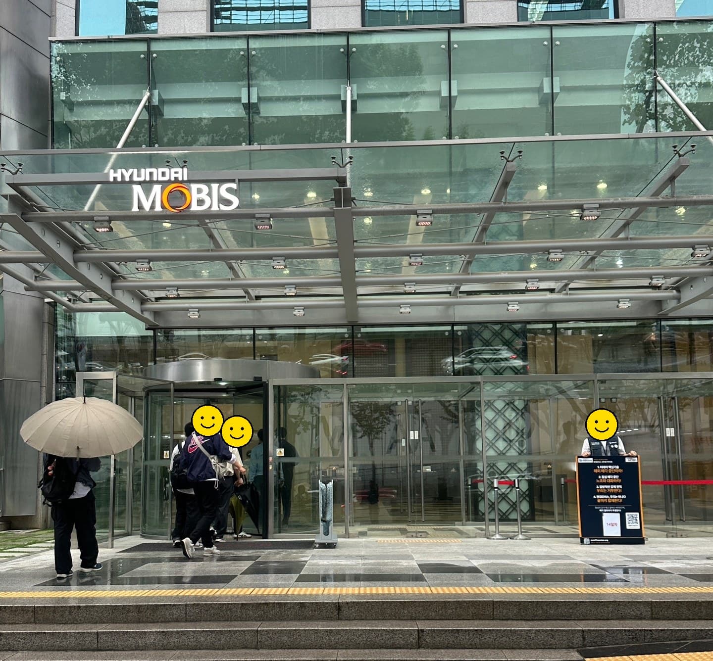현대모비스 본사 회전문 앞으로 출근하는 구성원들과 우측에 1인시위 폼보드를 든 조합원이 함께 보이는 14일차 광경