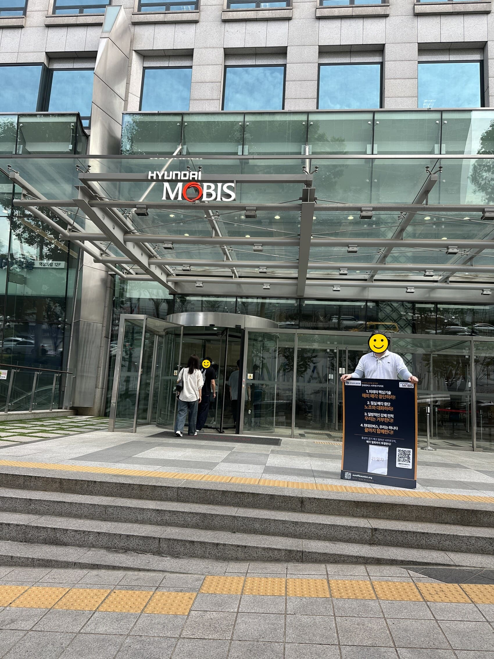 현대모비스 본사 정문 앞에서 네 가지 요구와 21일차 표시가 적힌 1인시위 폼보드를 들고 선 조합원의 21일차 광경