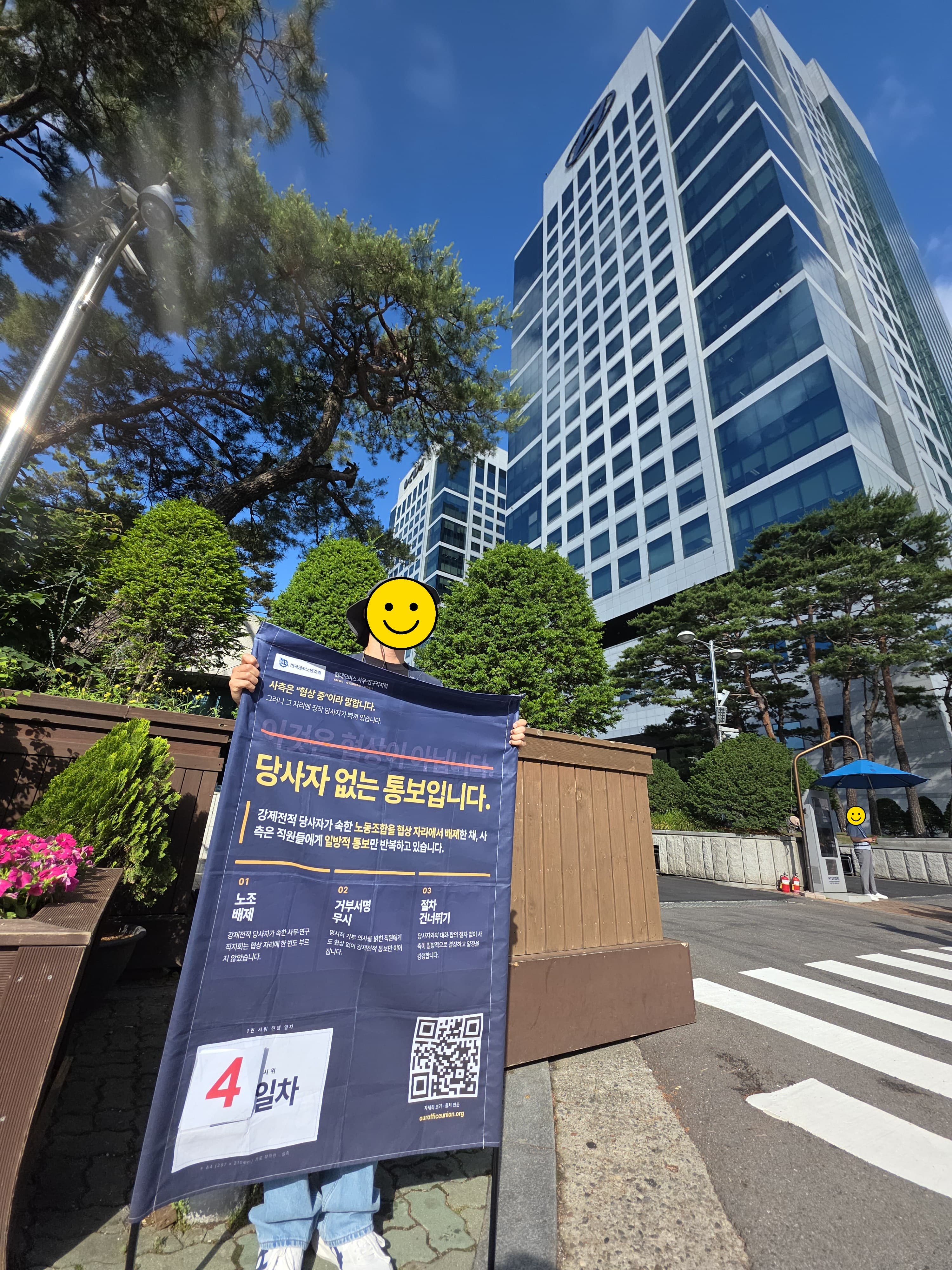 서울 양재동 현대자동차그룹 본사 앞에서 “당사자 없는 통보입니다 · 4일차” 폼보드를 들고 선 현대모비스 사무연구직지회 조합원의 모습 (얼굴은 스마일 이모지로 가림 처리)