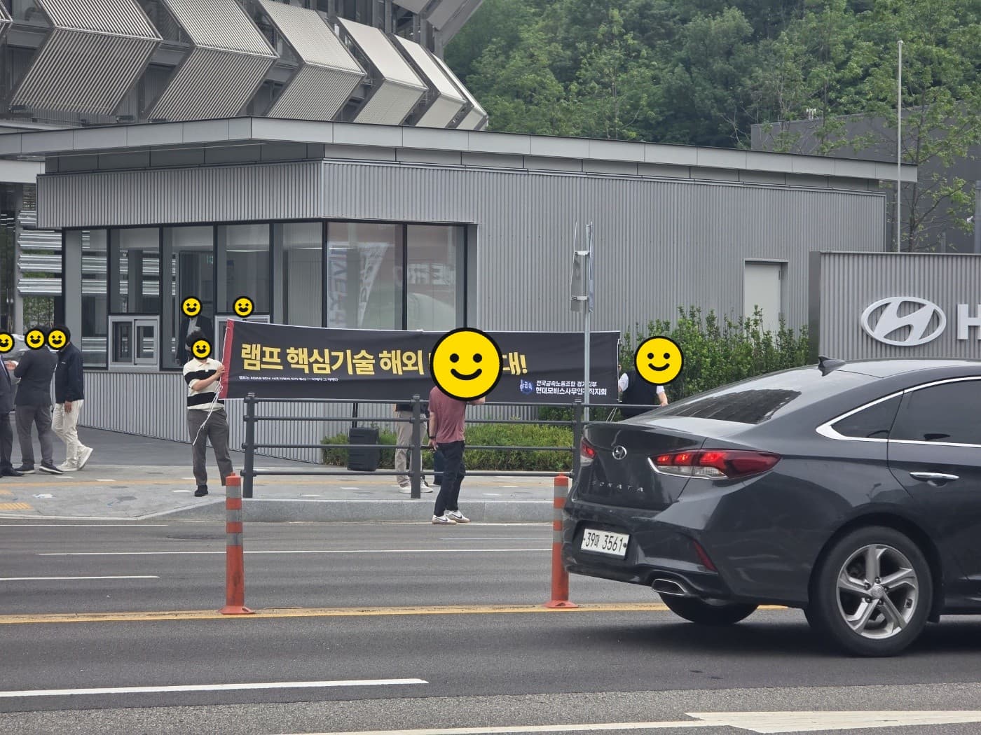 회장 차량 동선의 도로변에서 현수막을 펼친 조합원들과 통과하는 차량